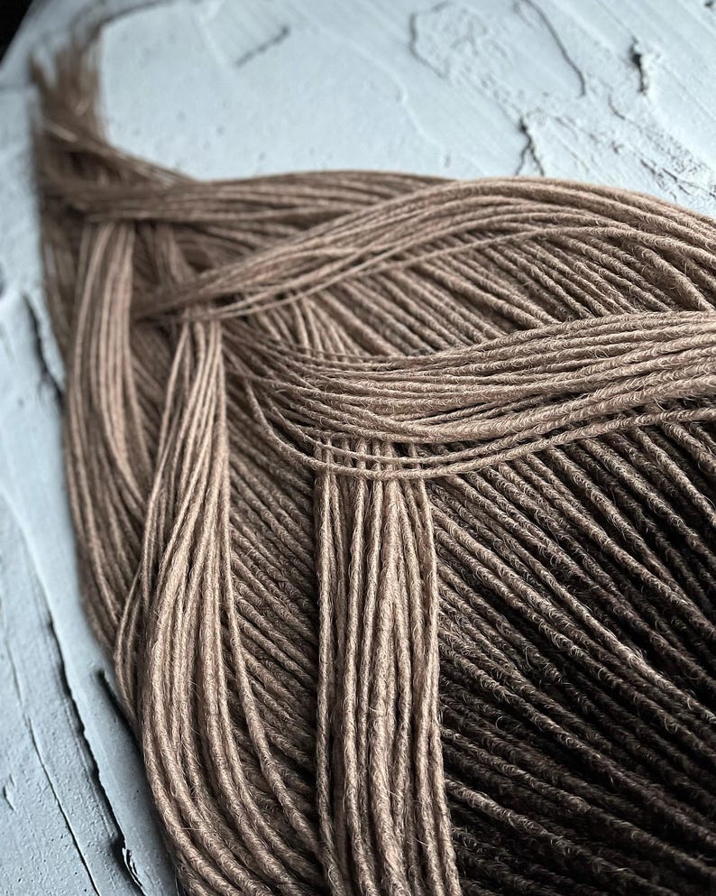 May include: A close-up of a bundle of brown and dark brown synthetic dreadlocks. The dreadlocks are arranged in a criss-cross pattern.