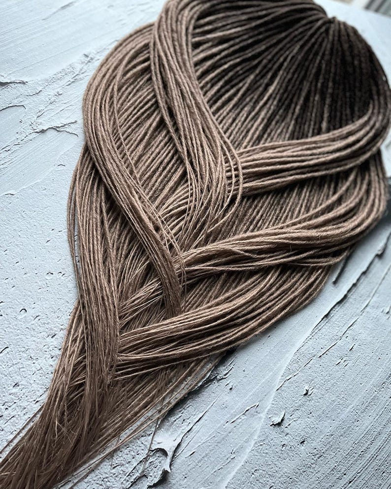 May include: A bundle of brown ombre synthetic dreadlocks. The dreadlocks are arranged in a loose braid pattern.