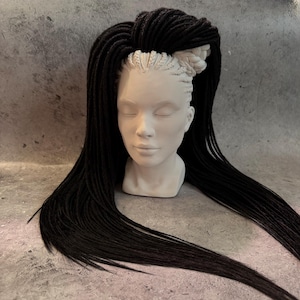 May include: A mannequin head with long black dreadlocks styled in a high ponytail. The dreadlocks are thick and evenly spaced.