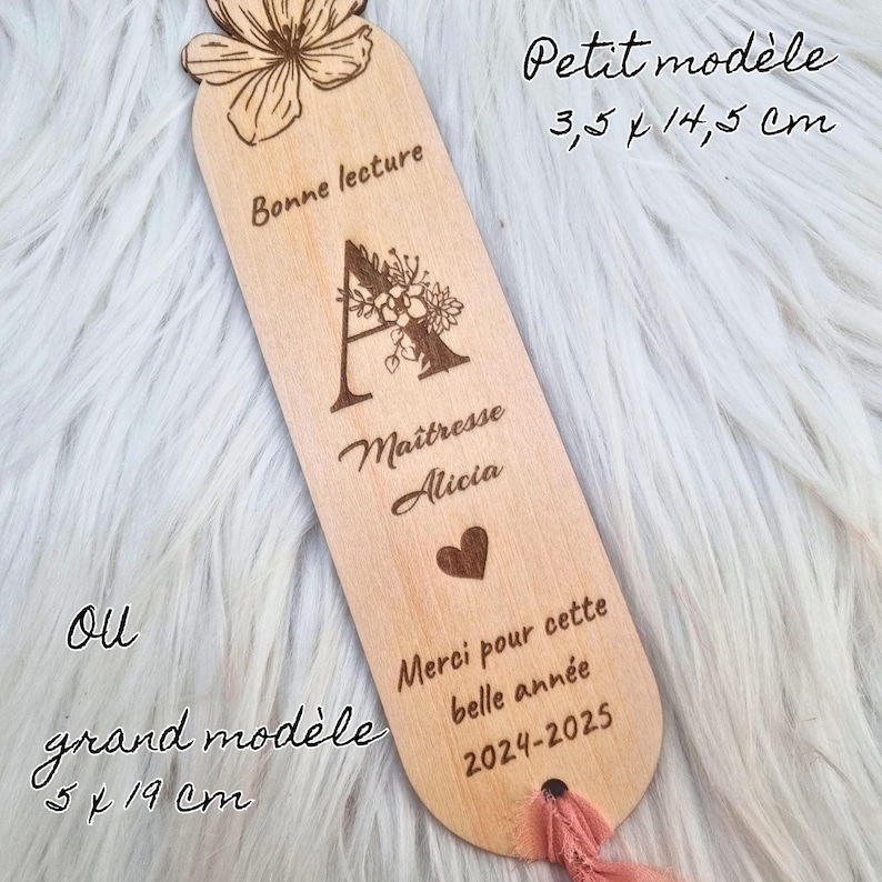 May include: A wooden bookmark with a floral design at the top and a pink ribbon. The bookmark has the text "Bonne lecture", "Ma&icirc;tresse Alicia", "Merci pour cette belle ann&eacute;e 2024-2025", and the dimensions 3.5 x 14.5 cm or 5 x 19 cm.