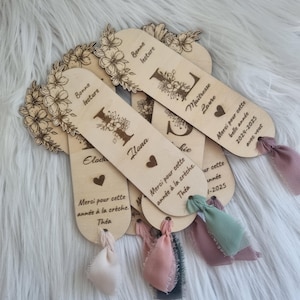 May include: Wooden bookmarks with floral designs and personalized text. Each bookmark features a decorative floral border, an initial, and a ribbon. The text includes names, phrases like "Bonne lecture," and dates.