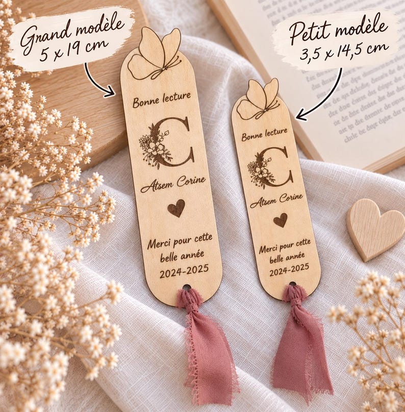 May include: Two light-colored wooden bookmarks with rounded tops, each featuring an engraved butterfly, a floral letter C, the text "Bonne lecture," "Atsem Corine," a heart, and "Merci pour cette belle ann&eacute;e 2024-2025." Each has a dusty pink fabric tassel.