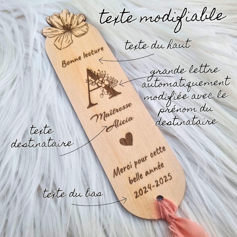 May include: A wooden bookmark with engraved text and a floral design. The bookmark features the words "Bonne lecture", "Ma&icirc;tresse Alicia", and "Merci pour cette belle ann&eacute;e 2024-2025". A pink ribbon is attached.