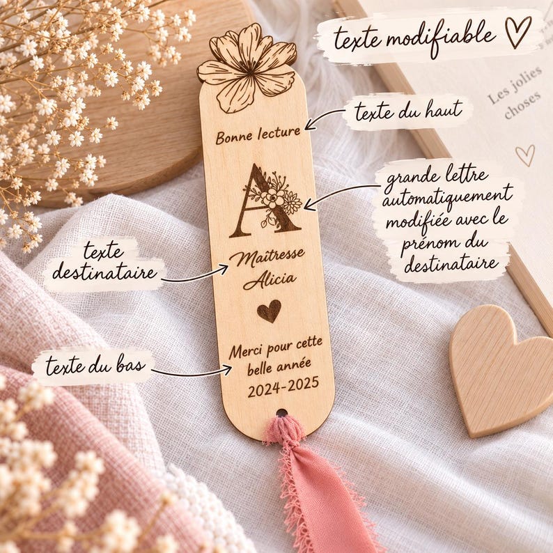 May include: A light-colored wooden bookmark featuring a laser-engraved flower at the top, the text Bonne lecture, a large letter A with floral details, the name Maitresse Alicia, a heart icon, the text Merci pour cette belle ann&eacute;e, and 2024-2025.