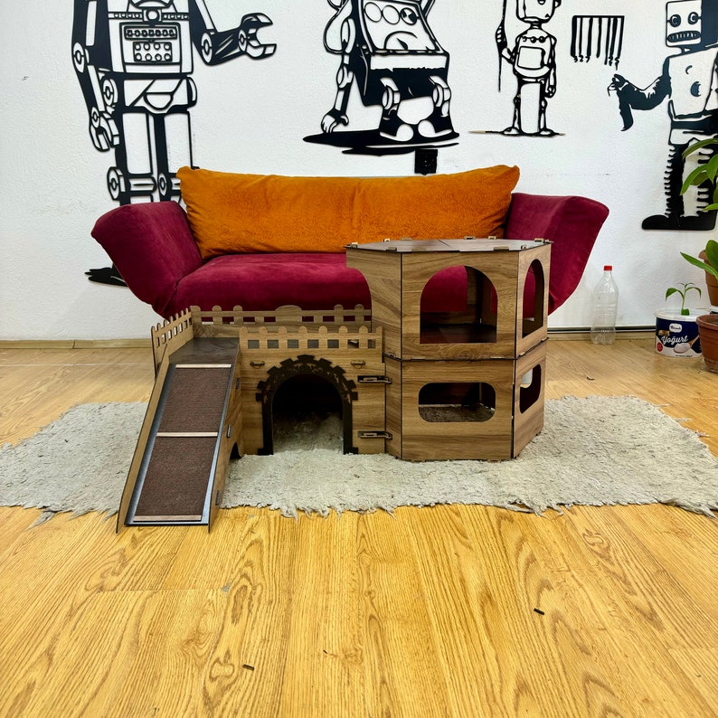 K&ouml;nnte beinhalten: Ein h&ouml;lzernes Katzenspielhaus mit einer Rampe, einem Tunnel und zwei Ebenen. Das Spielhaus ist braun und hat eine nat&uuml;rliche Holzoptik. Es steht auf einem hellbraunen Teppich vor einem roten Sofa.