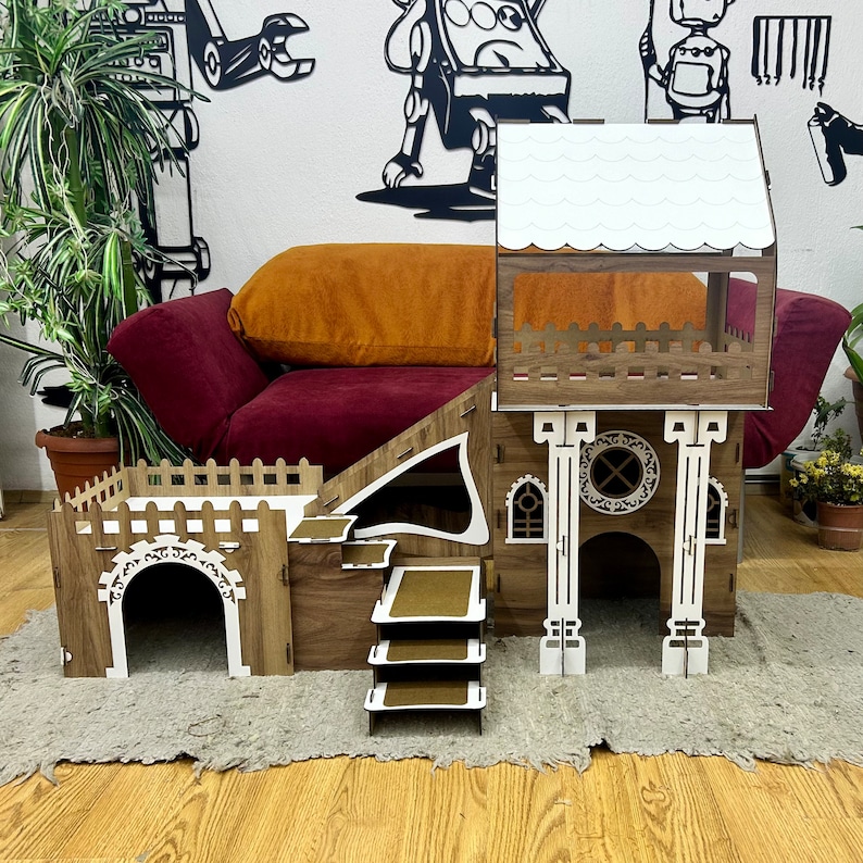 K&ouml;nnte beinhalten: Ein Katzenhaus aus Holz mit einem wei&szlig;en Dach, einer Rutsche und einer Plattform. Das Haus hat ein kleines Fenster und eine T&uuml;r. Das Haus ist aus Holz und hat eine braune Farbe.