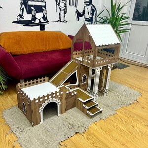 K&ouml;nnte beinhalten: Ein h&ouml;lzerner Katzenbaum mit einer Rampe, einer Plattform und einem Tunnel. Der Katzenbaum ist braun und wei&szlig; lackiert und hat ein wei&szlig;es Dach. Der Katzenbaum steht auf einem hellbraunen Holzboden.
