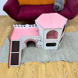 K&ouml;nnte beinhalten: Ein mehrst&ouml;ckiges Katzenhaus in Rosa und Wei&szlig; mit einer Rampe und einer kleinen &Ouml;ffnung. Das Haus ist aus Holz und hat ein modernes Design.