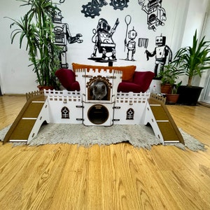 May include: A white cat castle playhouse with a grey cat inside. The castle has two ramps and a small opening for the cat to enter. The castle is made of wood and has a white paint finish.