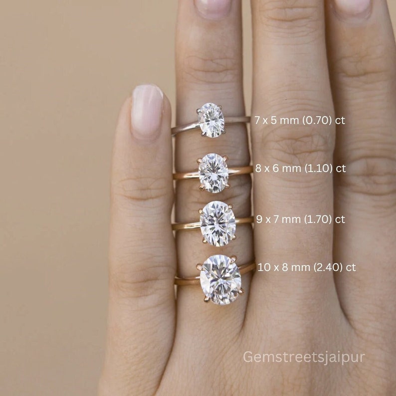 May include: A comparison of five oval-shaped diamond rings on a hand. The rings are set in gold and are arranged in order of size, with the smallest ring at the top and the largest ring at the bottom. The rings are labeled with their size in millimeters and carats. The text "Gemstreetsjaipur" is visible at the bottom of the image.