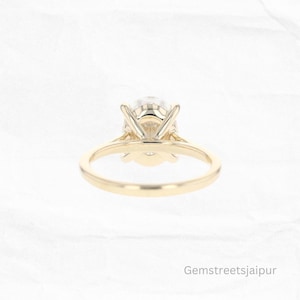 May include: A gold engagement ring with a round, clear center stone and a simple band. The ring is set with a prong setting.