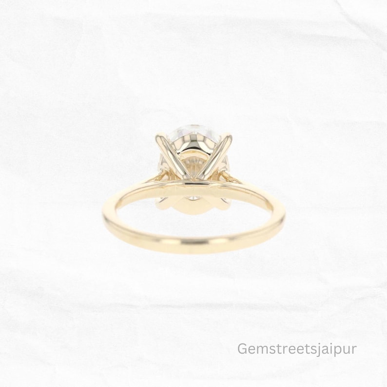 May include: A gold engagement ring with a round, clear center stone and a simple band. The ring is set with a prong setting.