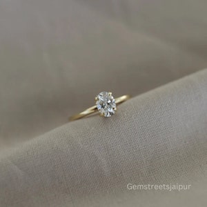 May include: A gold band ring with a single oval-shaped diamond.