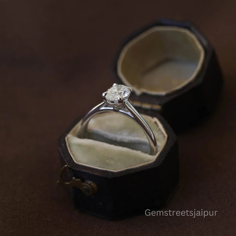 May include: A silver engagement ring with a round diamond in a black velvet ring box.