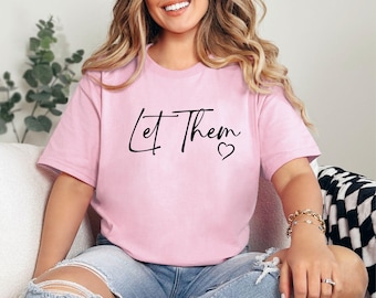 May include: A pink t-shirt with the text "Let Them" in black script with a small heart symbol.