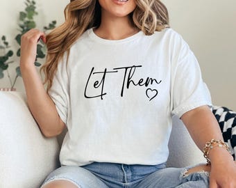 May include: White t-shirt with the text "Let Them" in black script with a small heart symbol.