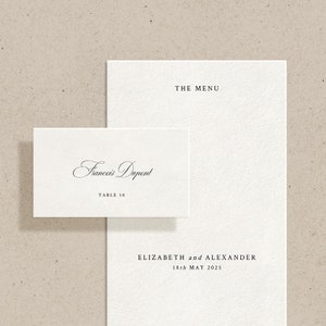 May include: A white place card with the name "Frances Dupont" and the text "Table 10" printed in black. The place card is next to a white menu card with the text "The Menu" at the top, followed by "Elizabeth and Alexander" and the date "13th May 2023". The bottom of the menu card reads "London, England".