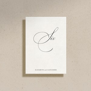 May include: A white card with the number "Six" written in elegant cursive script. The text "Elizabeth and Alexander" is printed below the number.