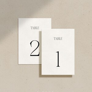 May include: Two white table number cards with black text. The card on the left says "TABLE 2" and the card on the right says "TABLE 1".