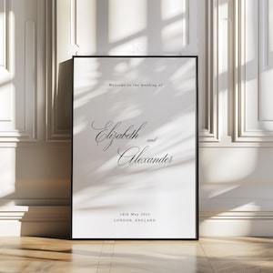 May include: A framed wedding welcome sign with the text "Welcome to the wedding of Elizabeth and Alexander" in elegant script. The date, May 18th, 2025, and location, London, England, are also displayed. The sign is in a black frame.
