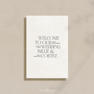 May include: A white card with black text that reads "Welcome to our wedding Millie & Cortez" with the date "Second of August Twenty Twenty-Four" and the location "London, United Kingdom".