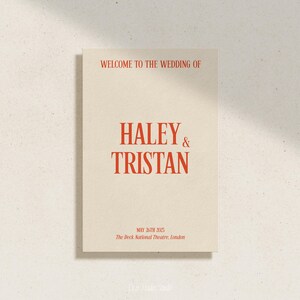May include: A wedding announcement card with a cream background and red text. The text reads "Welcome to the wedding of Haley & Tristan, May 26th 2025, The Deck National Theatre, London."