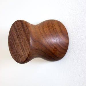 May include: A dark brown wooden hook with a rounded, bulbous shape. The hook is made of solid wood and has a natural, rustic finish.