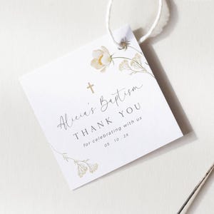 Puede incluir: Etiqueta de agradecimiento blanca con una cruz dorada y un diseño floral. El texto dice "El bautismo de Alicia Gracias por celebrar con nosotros 05.10.2X"