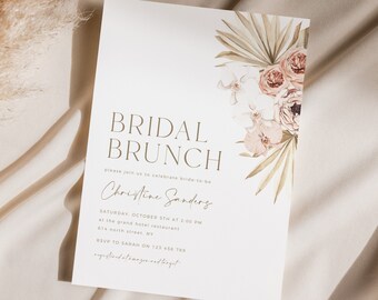May include: A white bridal brunch invitation with a gold border and text. The invitation features a watercolor illustration of palm leaves and pink and white flowers. The text reads "Bridal Brunch" and "Please join us to celebrate bride-to-be Christine Sanders".
