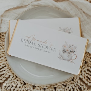 Puede incluir: Barra de chocolate blanco con envoltorio de papel de aluminio dorado. La barra tiene un diseño floral y el texto "Amanda's Bridal Shower Thanks for coming!" impreso en ella.