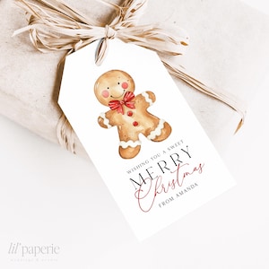 Könnte beinhalten: Ein weißes Geschenk-Etikett mit einer Aquarell-Illustration eines Lebkuchenmanns und dem Text "Wishing you a sweet Merry Christmas from Amanda". Das Etikett ist an einem verpackten Geschenk mit einer Raffia-Schleife befestigt.