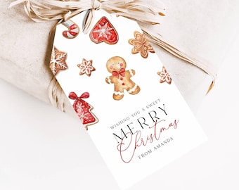 May include: A white gift tag with watercolor illustrations of gingerbread cookies and candy canes. The tag reads "Wishing you a sweet Merry Christmas from Amanda" in black and red script. The tag is tied to a wrapped gift with natural raffia.