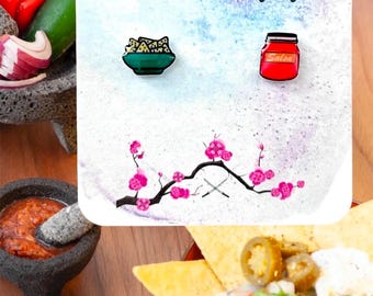 May include: A set of three enamel pins featuring a bowl of chips, a jar of salsa, and a stylized cherry blossom branch with two crossed swords. The pins are on a white background with a watercolor effect.