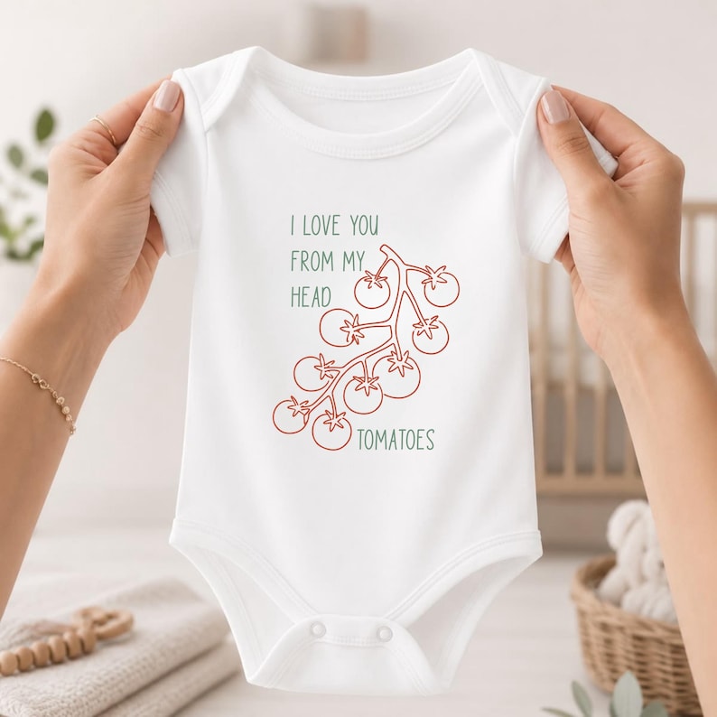 May include: A white short-sleeved baby bodysuit featuring a red line-art illustration of a vine of tomatoes. The text printed in green reads I LOVE YOU FROM MY HEAD TO-MA-TOES, with the word TOMATOES positioned below the tomato illustration.