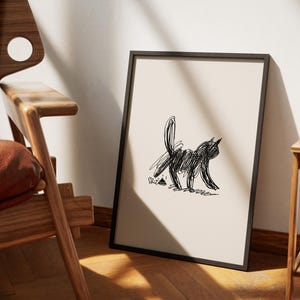 Könnte beinhalten: Abstrakter Schwarz-Weiß-Katzenkunstdruck in einem schwarzen Rahmen. Das Kunstwerk zeigt eine gekritzelte Katzenillustration auf beigem Hintergrund. Die gerahmte Kunst lehnt an einer Wand, neben einem Holzstuhl.