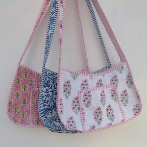 Könnte beinhalten: Drei gesteppte Umhängetaschen mit Blumenmustern in Rosa, Blau und Weiß. Jede Tasche hat passende Träger und rosa Besatz. Die rosa Tasche hat ein gelbes Blumendesign, die blaue Tasche ein blaues Blätterdesign und die weiße Tasche ein rosa Blumendesign.