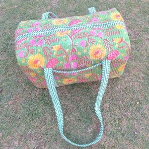 May include: A green and white striped duffel bag with a floral print. The bag has two long straps and a zipper closure.