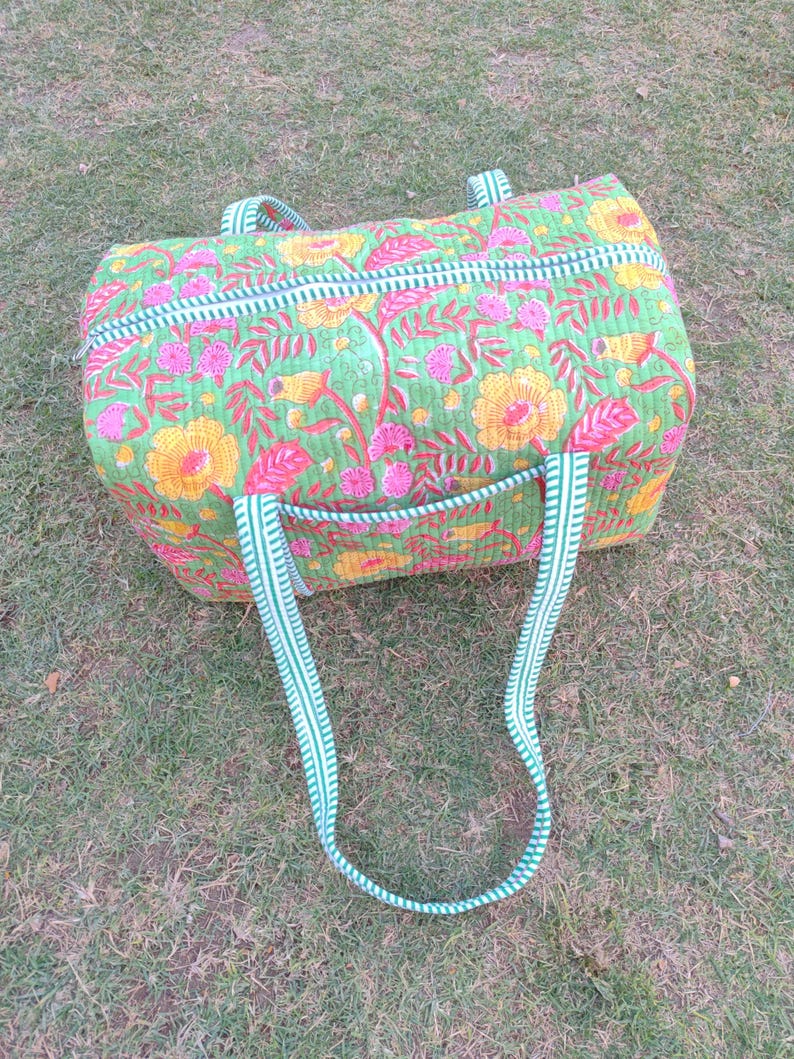 May include: A green and white striped duffel bag with a floral print. The bag has two long straps and a zipper closure.