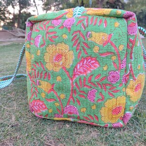 May include: A green, pink, and yellow floral print tote bag with a white and green striped handle.