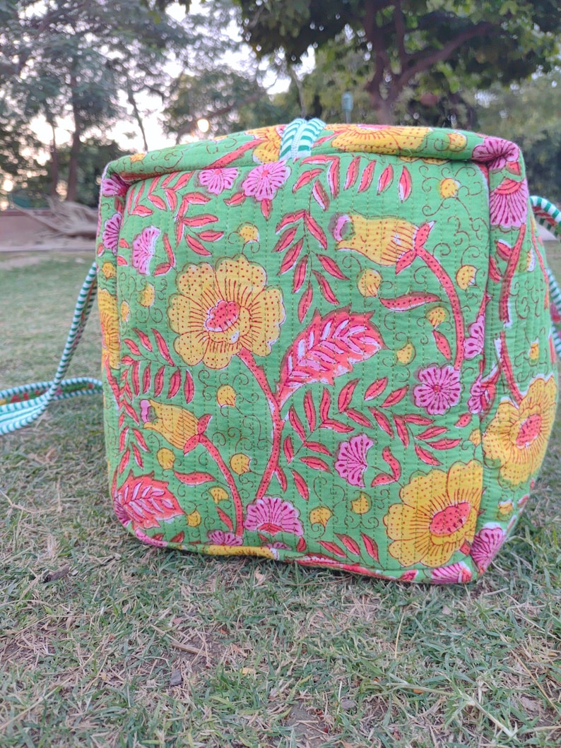 May include: A green, pink, and yellow floral print tote bag with a white and green striped handle.