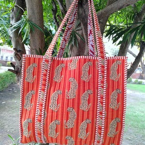 Könnte beinhalten: Eine große orangefarbene Tragetasche mit weißen Streifen und Leopardenmuster. Die Tasche hat zwei lange Henkel und ist aus gestepptem Stoff.