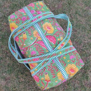 May include: A green and pink floral print duffel bag with white and green striped straps. The bag has a zipper closure and is made of quilted fabric.