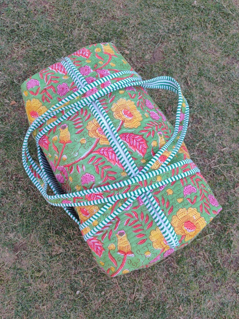 May include: A green and pink floral print duffel bag with white and green striped straps. The bag has a zipper closure and is made of quilted fabric.