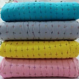 May include: Four fabric swatches stacked on top of each other. The top swatch is turquoise blue, the second is light gray, the third is yellow, and the bottom is pink. All four swatches have a small cross pattern.