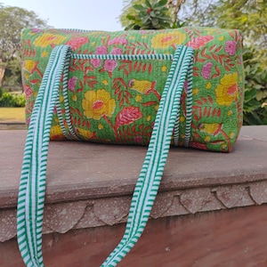 May include: A green quilted tote bag with floral and bird print. The bag has white and green striped handles.