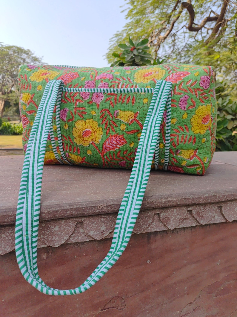 May include: A green quilted tote bag with floral and bird print. The bag has white and green striped handles.