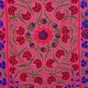 May include: A pink fabric with intricate embroidery featuring red and blue floral designs. The fabric has a central motif with a circular pattern and is surrounded by repeating floral patterns.