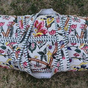 May include: A white canvas duffel bag with a floral print and green and white striped trim. The bag has two handles and a zipper closure.
