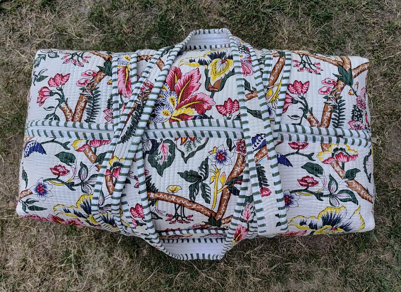 May include: A white canvas duffel bag with a floral print and green and white striped trim. The bag has two handles and a zipper closure.