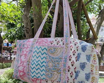 Peut inclure: Un sac de voyage matelassé en patchwork avec des motifs floraux roses, bleus et blancs. Le sac a deux longues sangles et est suspendu à une branche d'arbre.